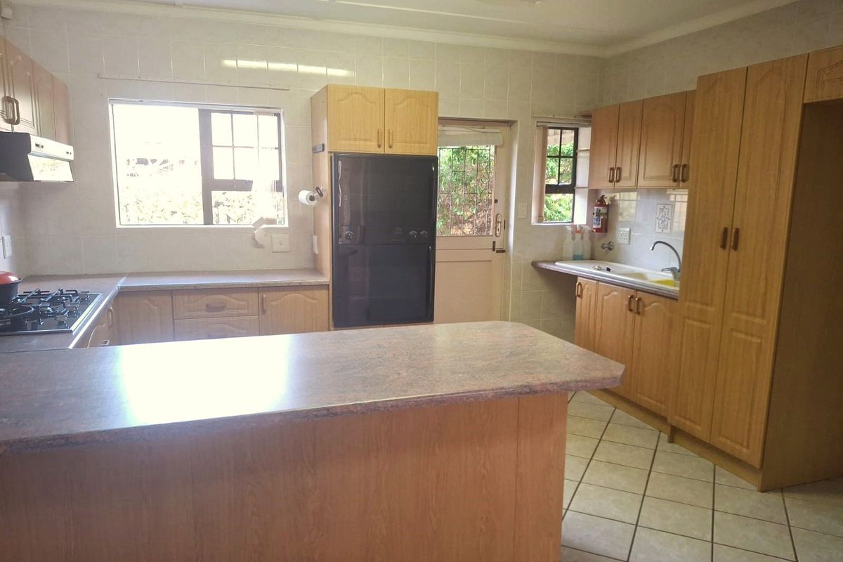 A functional kitchen featuring wood-look cabinetry, a central island, built-in oven, gas hob, and tiled flooring with direct access to the exterior.