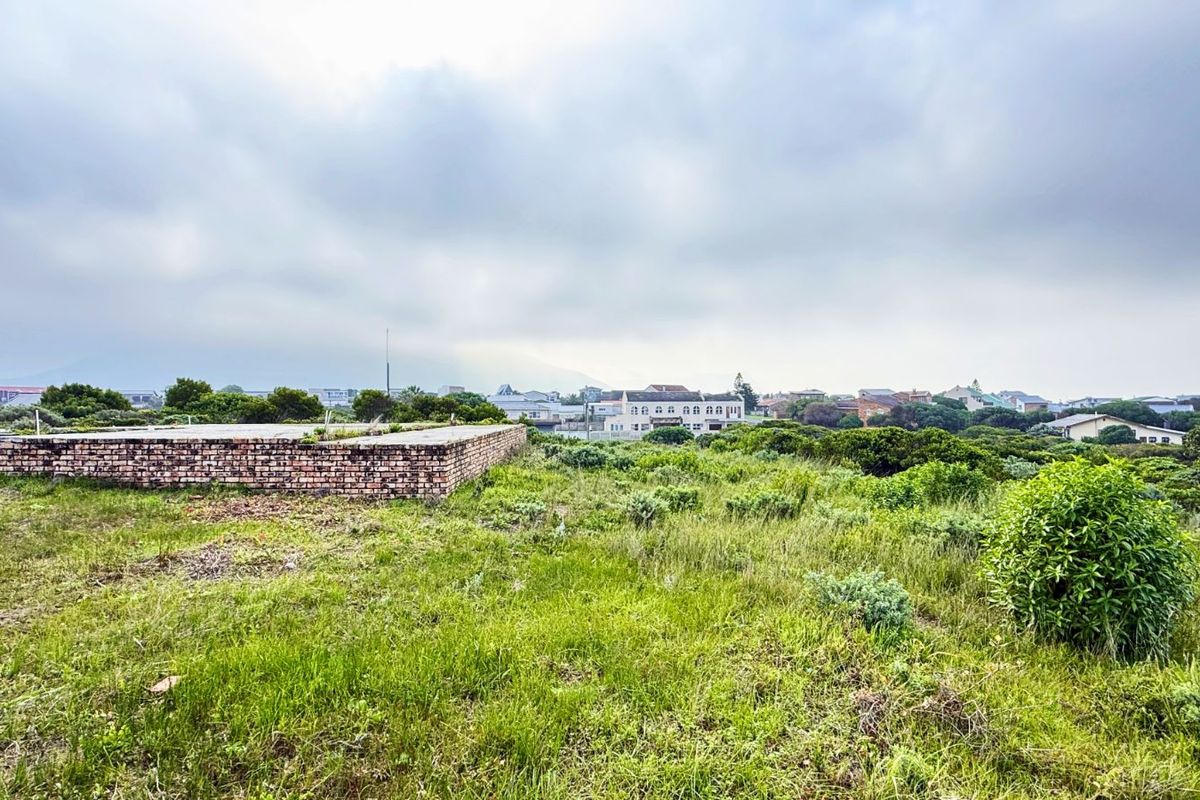 A vacant residential plot featuring an existing brick foundation slab, surrounded by natural coastal vegetation with views of the surrounding neighborhood.