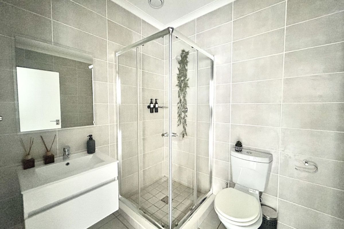 Modern bathroom featuring a glass-enclosed shower, wall-mounted vanity with basin, and a standard toilet, finished with neutral floor-to-ceiling wall tiles.