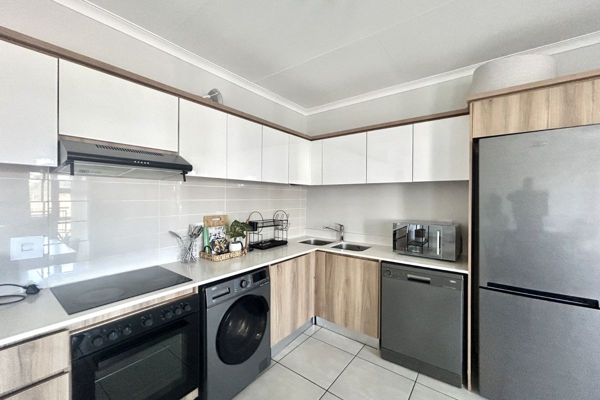 Modern kitchen featuring sleek white and wood-grain cabinetry, integrated appliances, tiled backsplash, and durable floor tiles.