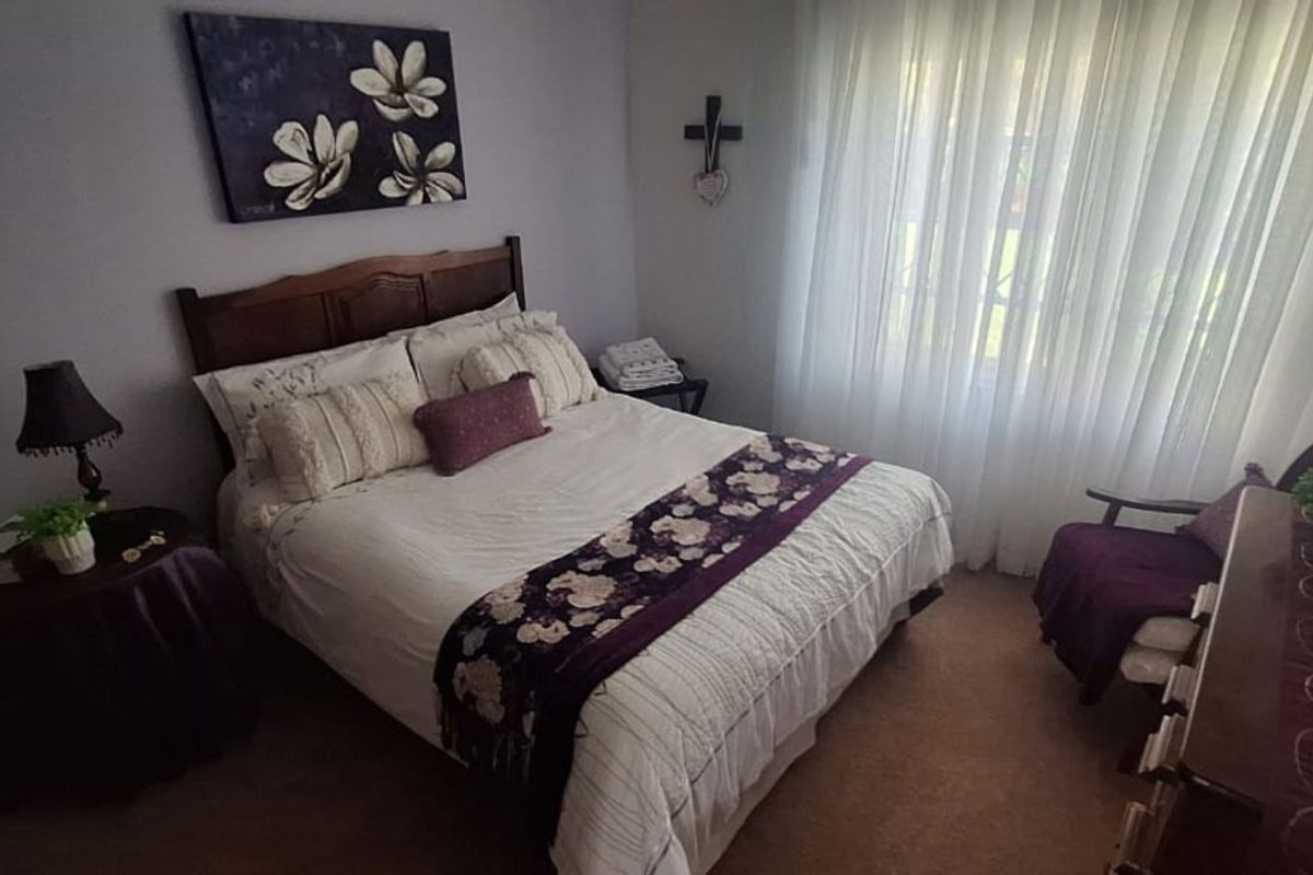 A cozy bedroom featuring carpeted flooring and large windows with sheer curtains, providing natural light and a comfortable living space.