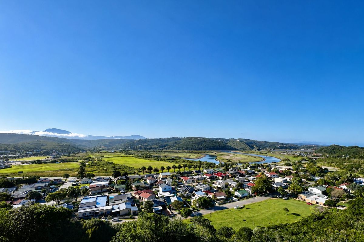 An elevated aerial view overlooking a residential neighborhood, green fields, and a winding river leading toward distant mountains.