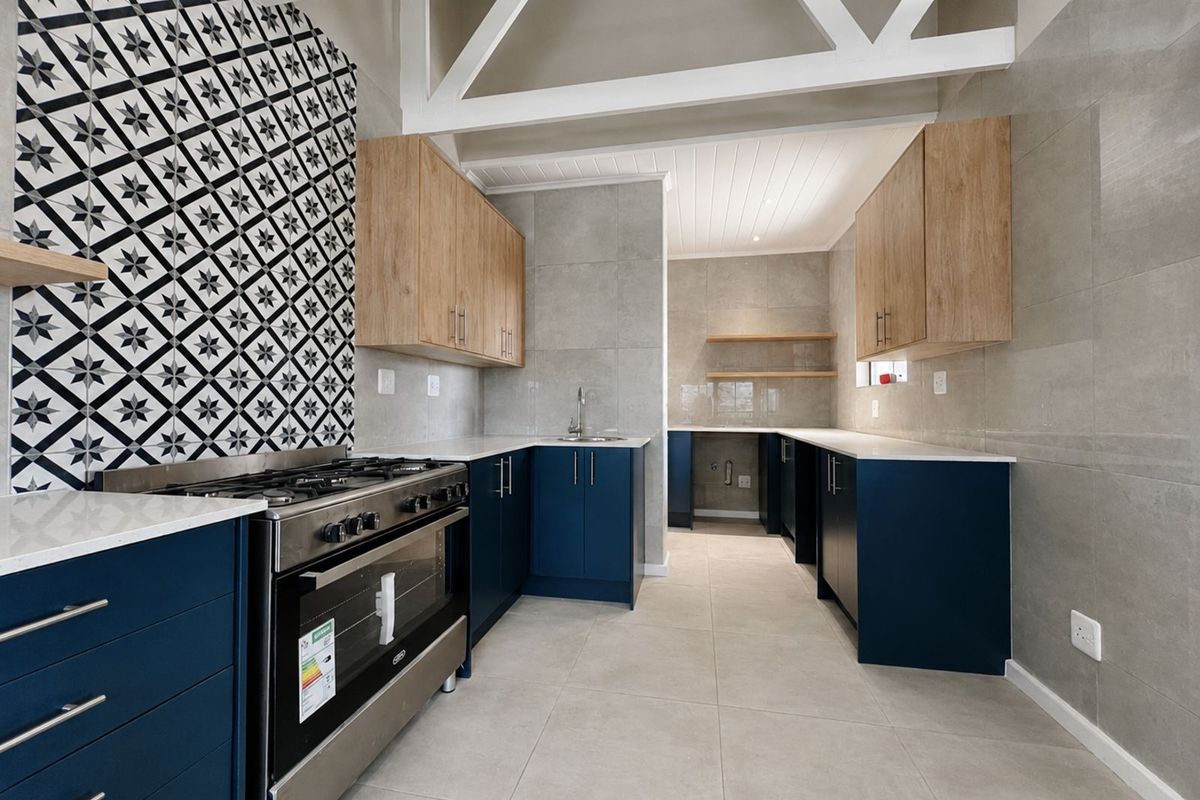 Modern kitchen featuring navy blue cabinetry, light wood upper cabinets, stone countertops, a gas stove, and decorative patterned tile backsplash.