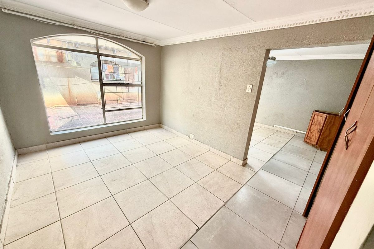 An empty living area featuring large arched windows, tiled flooring, and neutral wall finishes, providing a blank canvas for interior design.