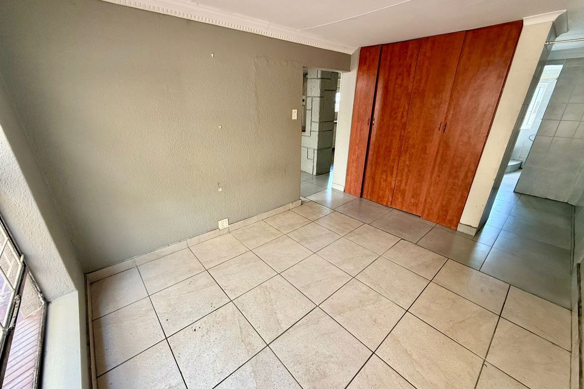 A bedroom featuring tiled flooring, built-in wooden cupboards, and crown molding, offering a functional space with direct access to adjacent areas.