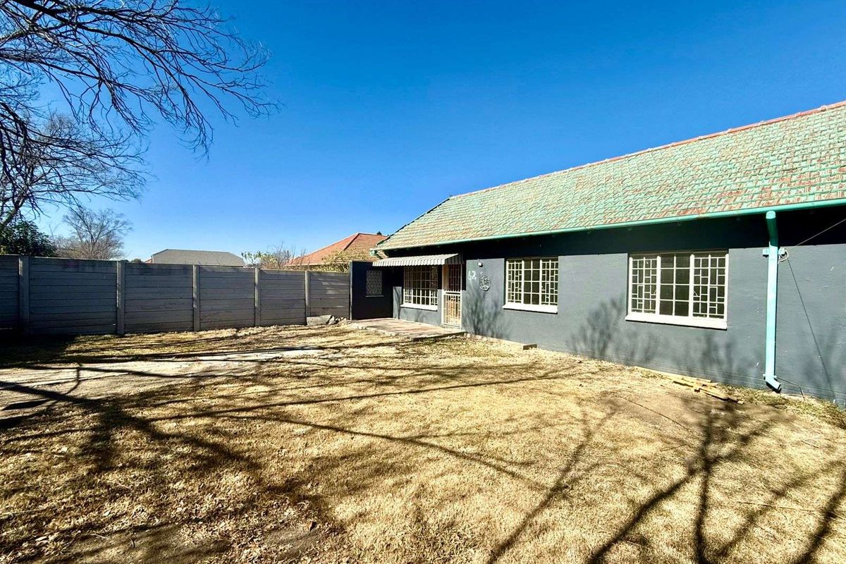 A view of the rear exterior of the house, featuring a large yard, concrete patio area, and a tiled roof.