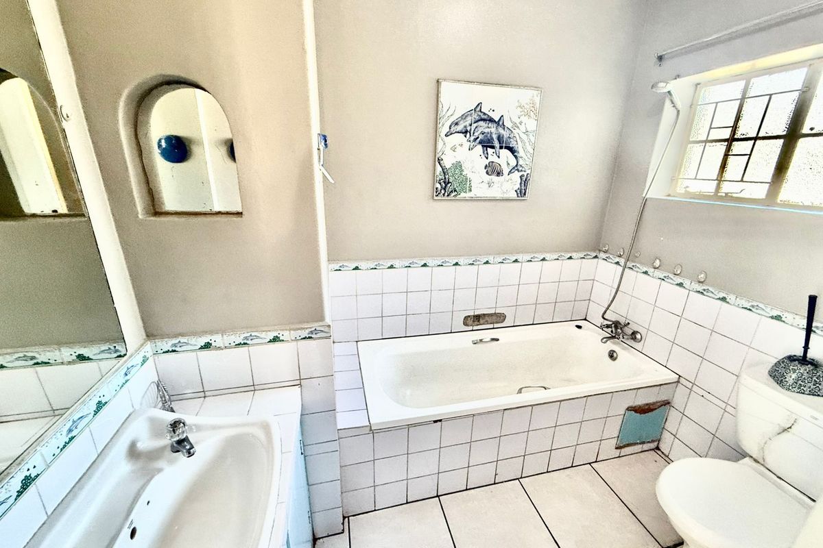 A dated bathroom featuring a built-in bathtub with shower mixer, pedestal basin, and tiled flooring.