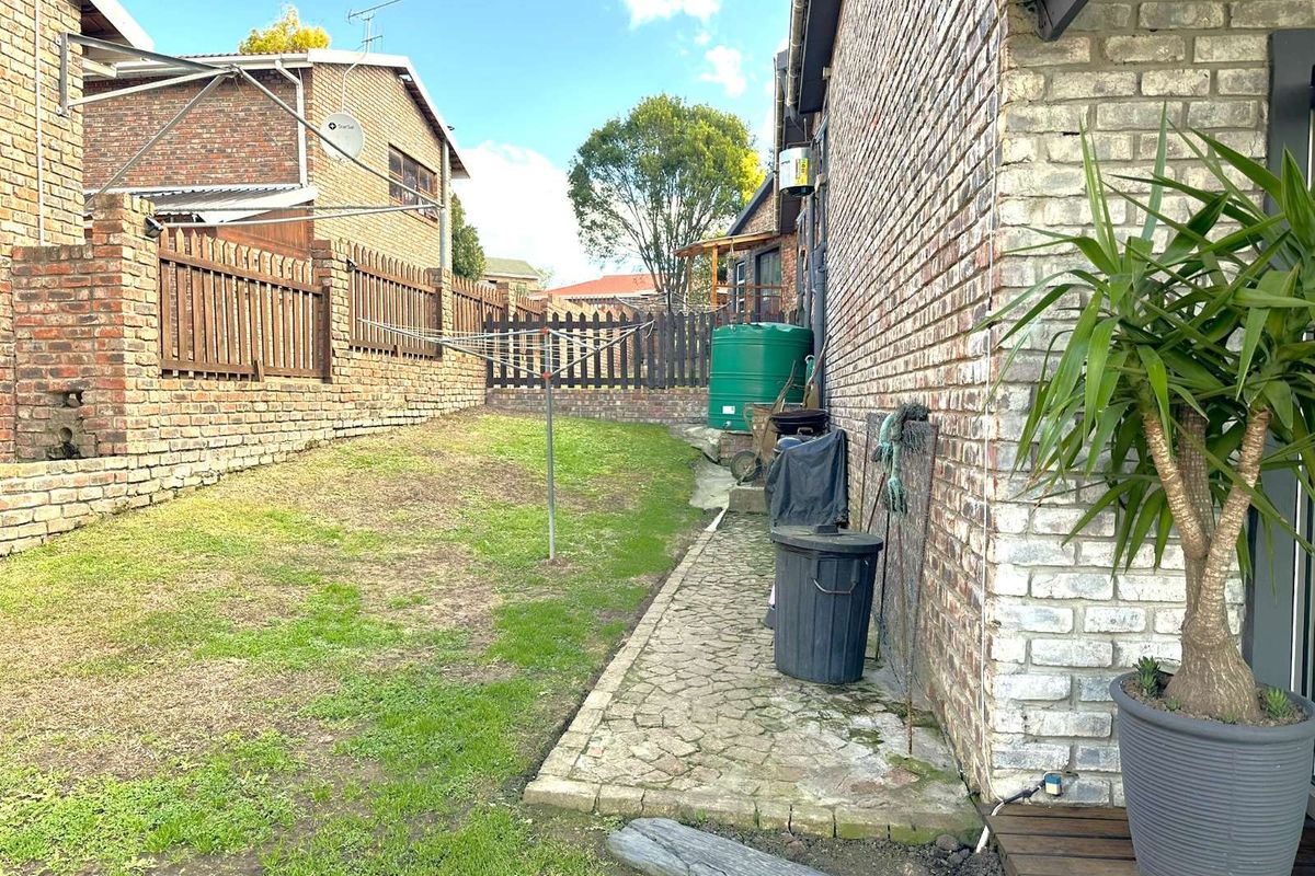 A side garden area featuring a paved walkway, brick boundary walls, a water tank, and a rotary clothesline.