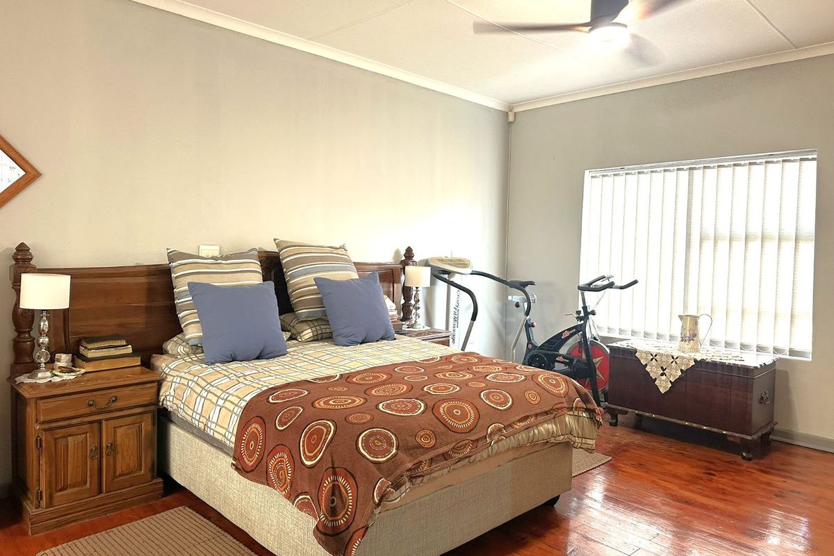 Spacious bedroom featuring polished timber flooring, vertical window blinds, and a ceiling fan.