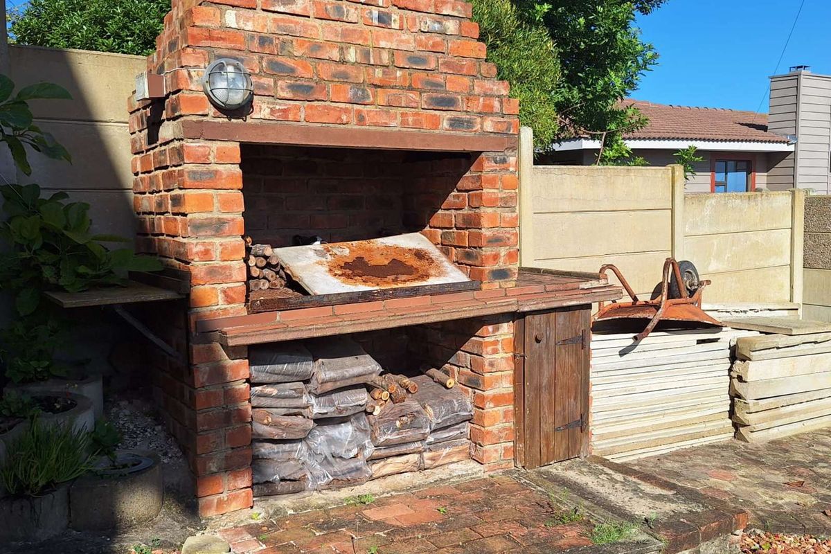 Outdoor brick-built barbecue area featuring a chimney, integrated storage, and paved surround, situated in a rear garden setting.