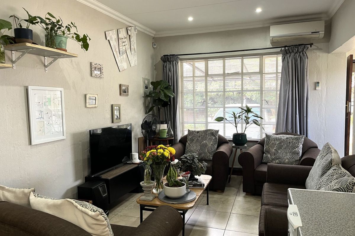 A comfortable living room featuring tiled flooring, a wall-mounted air conditioning unit, and large windows with blinds, providing a bright and functional living space.