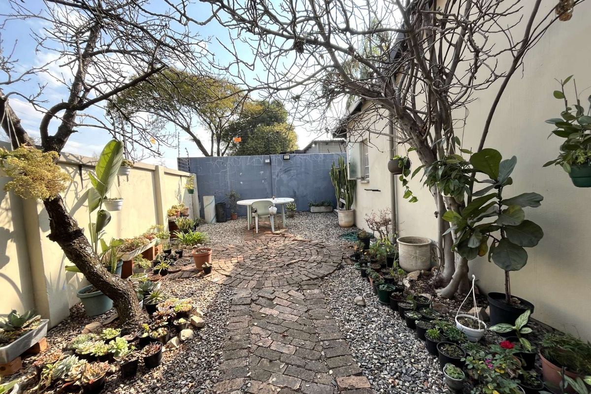 A private rear courtyard featuring a brick-paved pathway, gravel landscaping, and established trees, enclosed by high boundary walls.