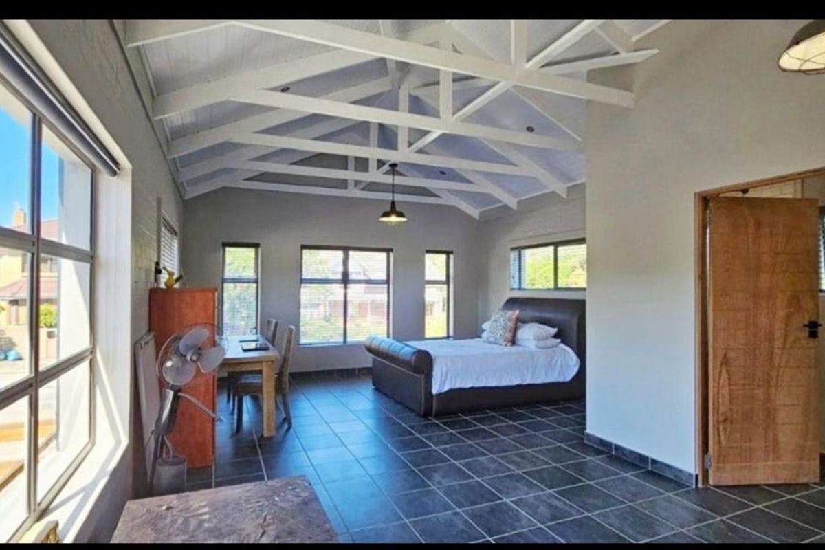 Spacious bedroom featuring high vaulted ceilings with exposed white trusses, large windows, and dark tiled flooring.