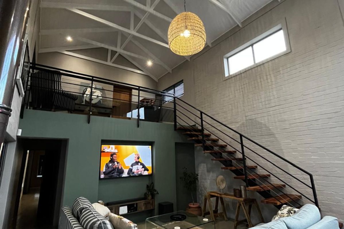 Spacious double-volume living area featuring exposed roof trusses, a mezzanine level, a feature staircase, and polished concrete flooring.