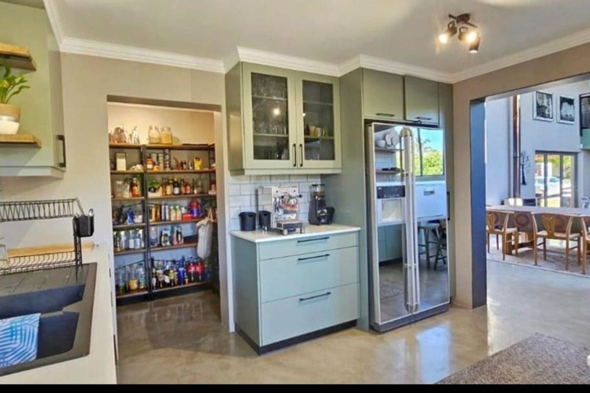 Modern kitchen featuring sage green cabinetry, a double basin sink, integrated refrigerator, and a convenient walk-in pantry with open shelving.