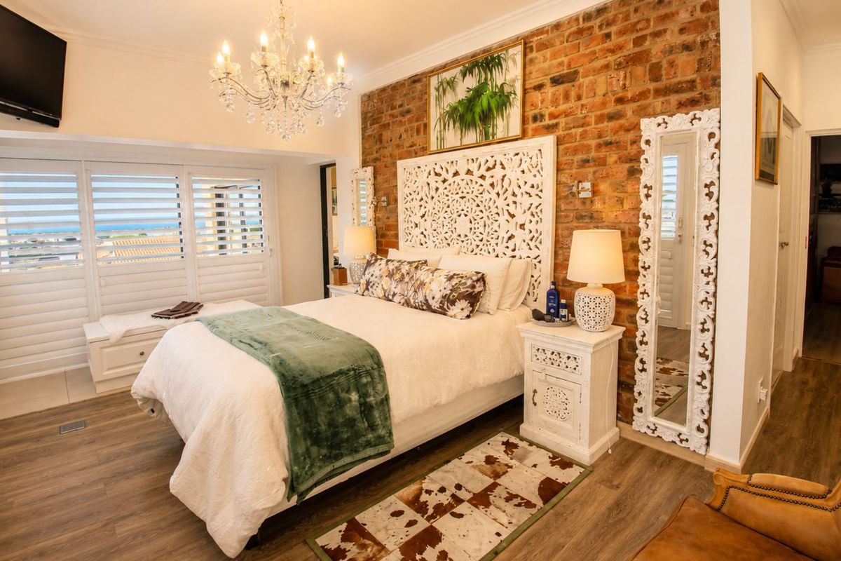A well-appointed bedroom featuring a rustic exposed brick feature wall, laminate flooring, and plantation shutters opening to a view.