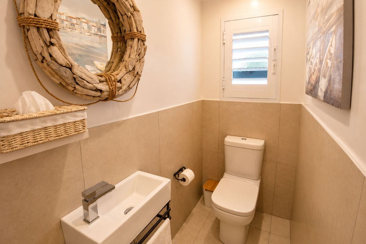 A compact, modern guest bathroom featuring neutral wall tiling, a wall-mounted basin with chrome faucet, and a white toilet.