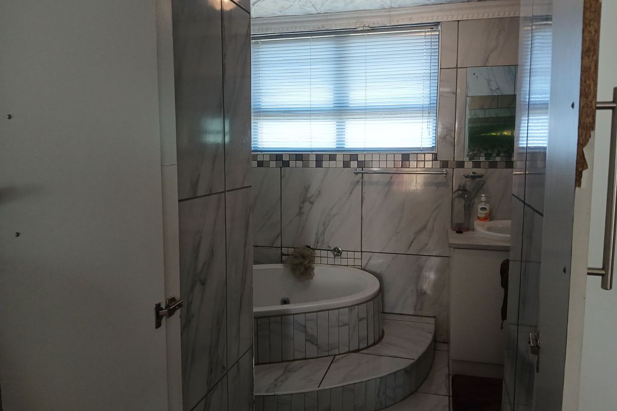 A bathroom featuring a raised corner bathtub with marble-look tiling, a vanity basin, and a window with fitted blinds.