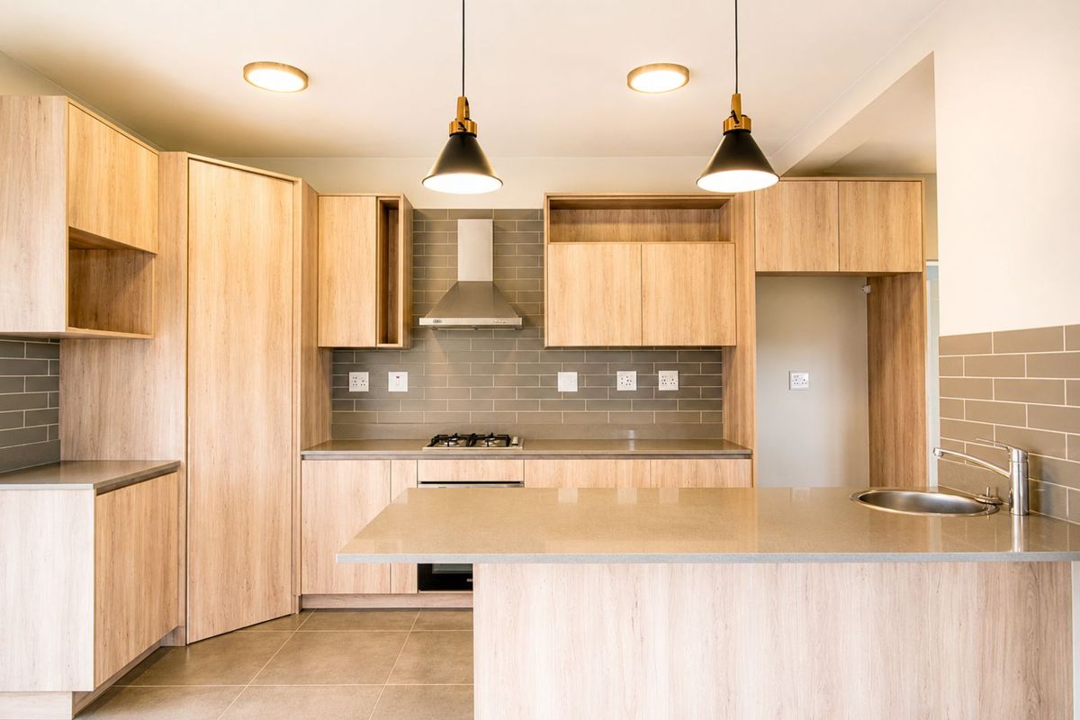Modern kitchen featuring light wood cabinetry, stone countertops, a built-in gas hob, stainless steel extractor fan, and a breakfast bar island.