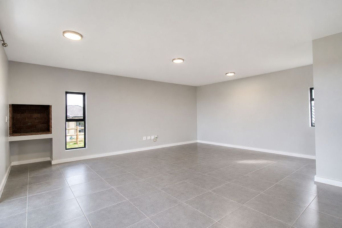 Spacious open-plan living area featuring neutral grey floor tiles, recessed ceiling lighting, and a built-in brick fireplace.