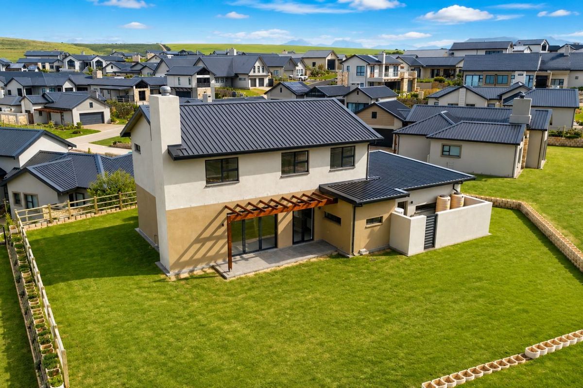 Aerial view of a modern two-story residential home featuring a metal roof, exterior chimney, and a rear patio with a wooden pergola.