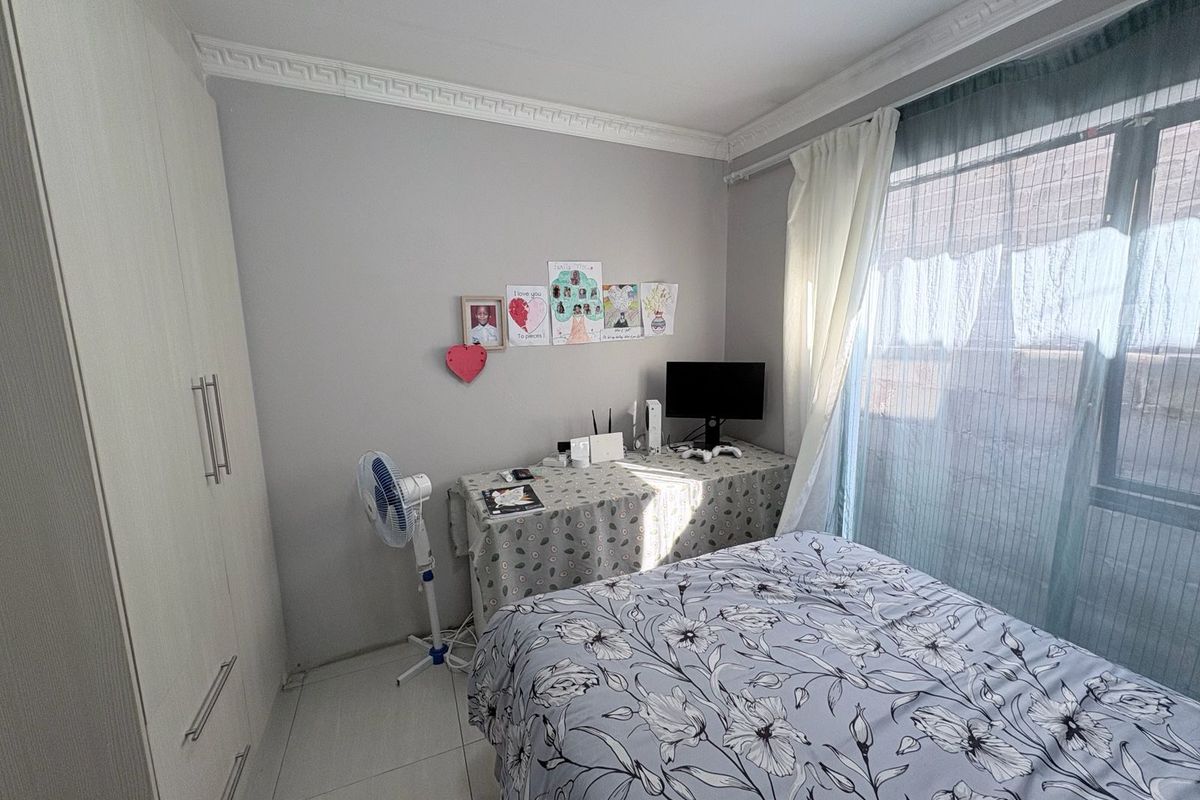 A bedroom featuring built-in cupboards, tiled flooring, and decorative ceiling cornicing, with natural light provided by a large window.