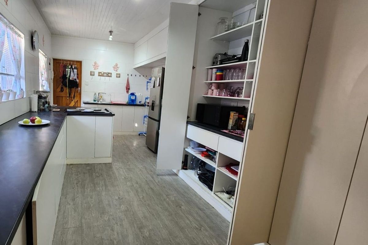 A functional kitchen featuring laminate countertops, built-in cabinetry, and a dedicated pantry storage unit with open shelving.