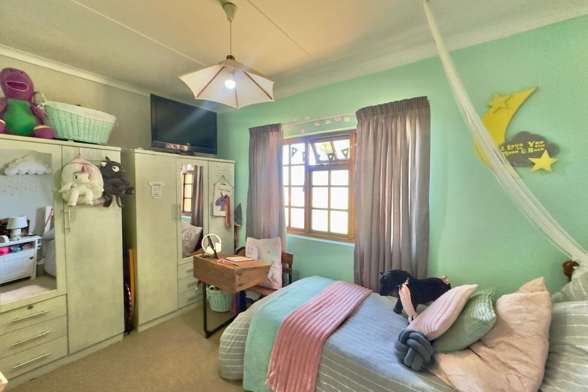 A bedroom featuring light green walls, a window with wooden frames, and built-in wardrobe cabinetry.