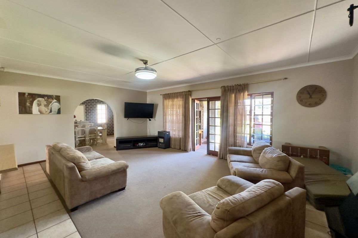 Spacious living room featuring neutral carpeting, a ceiling fan, and direct access to the outdoor patio area through glass-paneled doors.