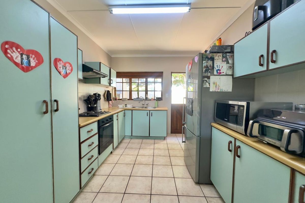 A functional galley-style kitchen featuring light-toned cabinetry, tiled flooring, built-in oven, hob, and extractor fan with direct access to the exterior.
