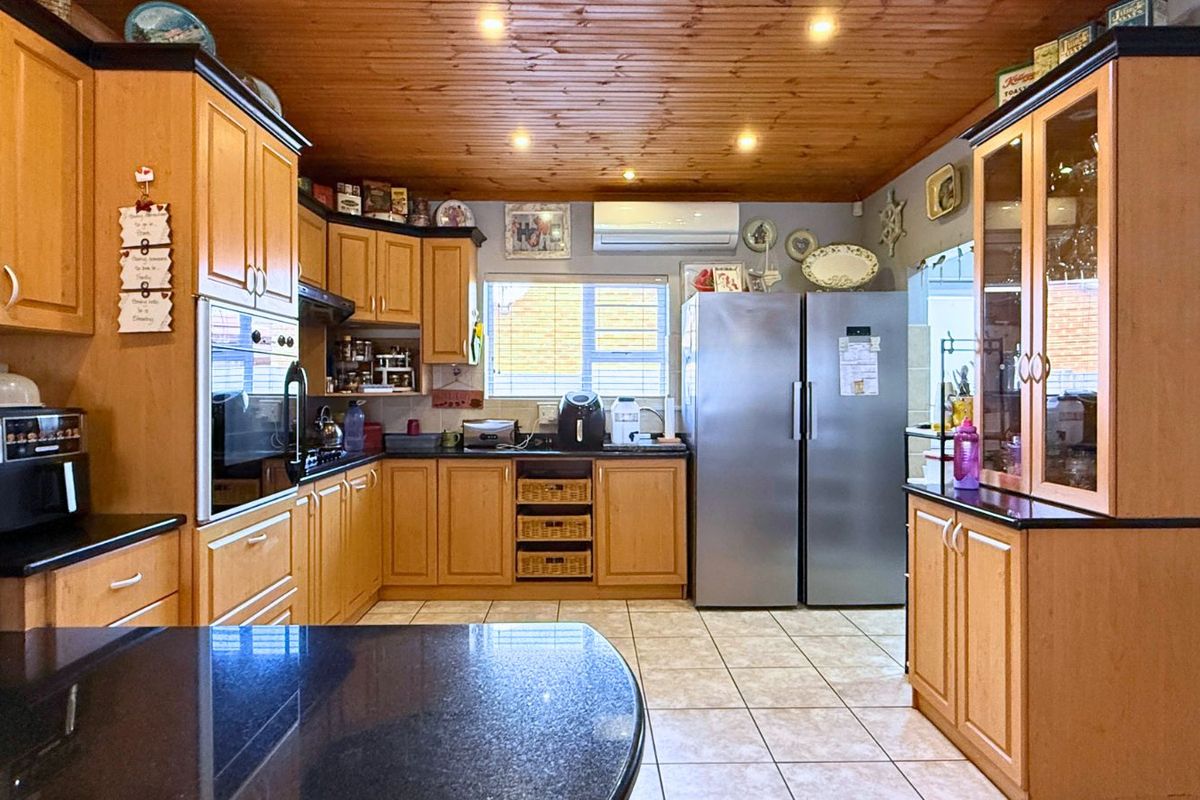 A functional kitchen featuring wooden cabinetry, dark granite countertops, tiled flooring, and a timber-paneled ceiling with integrated downlights.