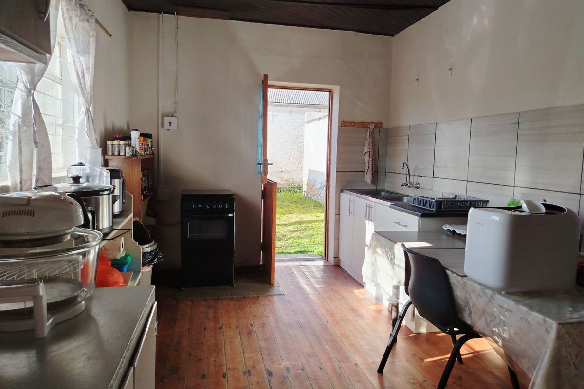 A functional kitchen featuring timber flooring, tiled splashbacks, a built-in sink, and direct access to the rear garden area.