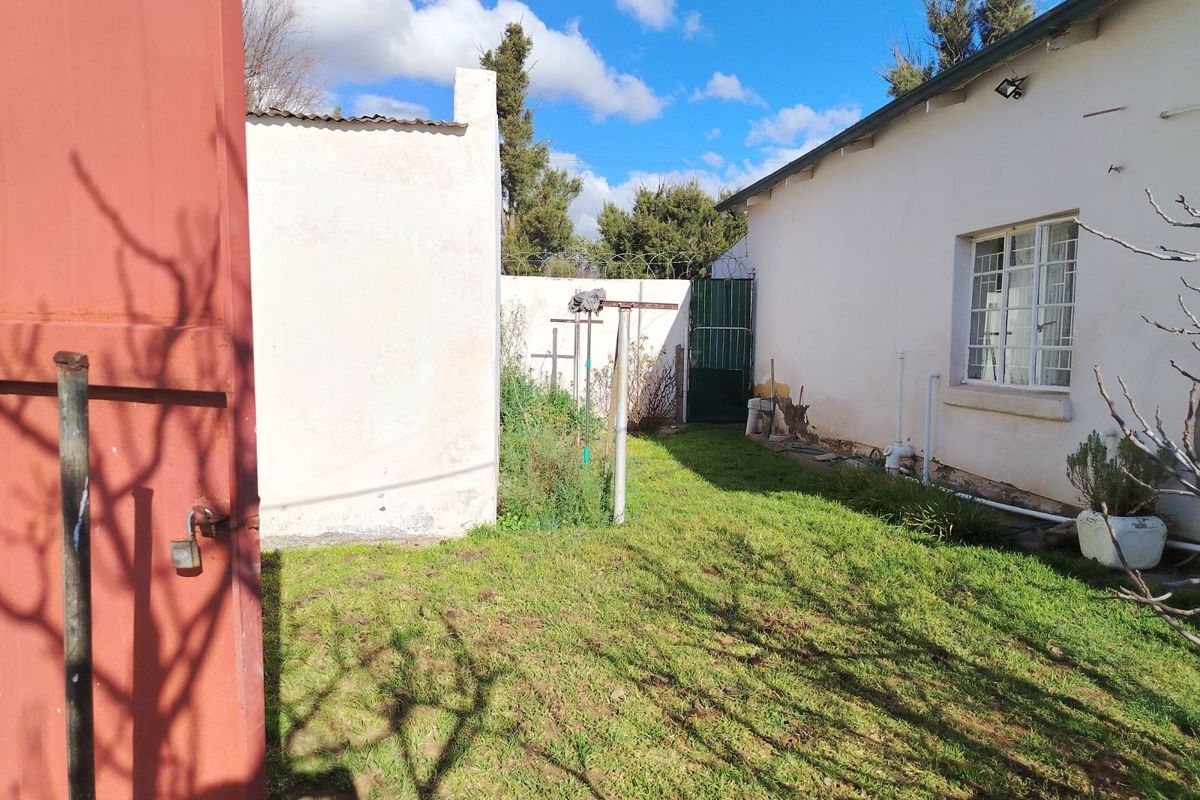 A view of the rear exterior area featuring a small lawn, perimeter walls with security fencing, and access to the side of the house.
