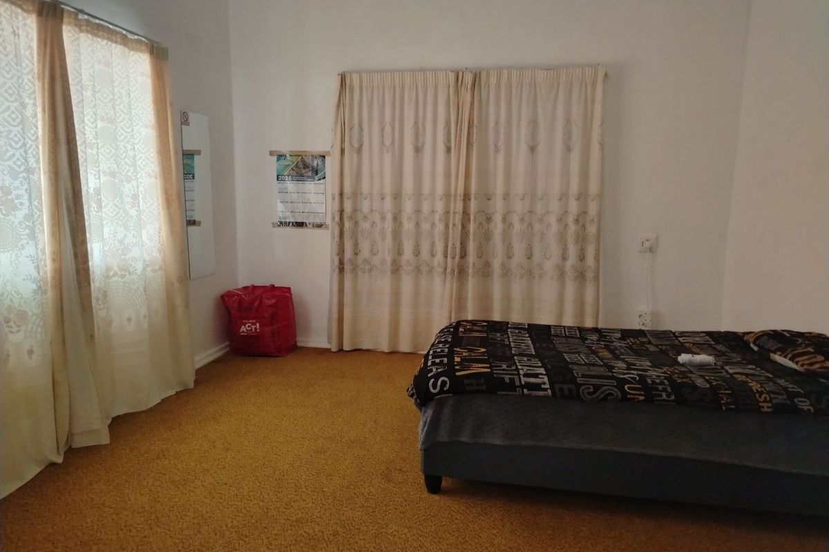 A bedroom featuring carpeted flooring, dual window curtains, and standard electrical fixtures.