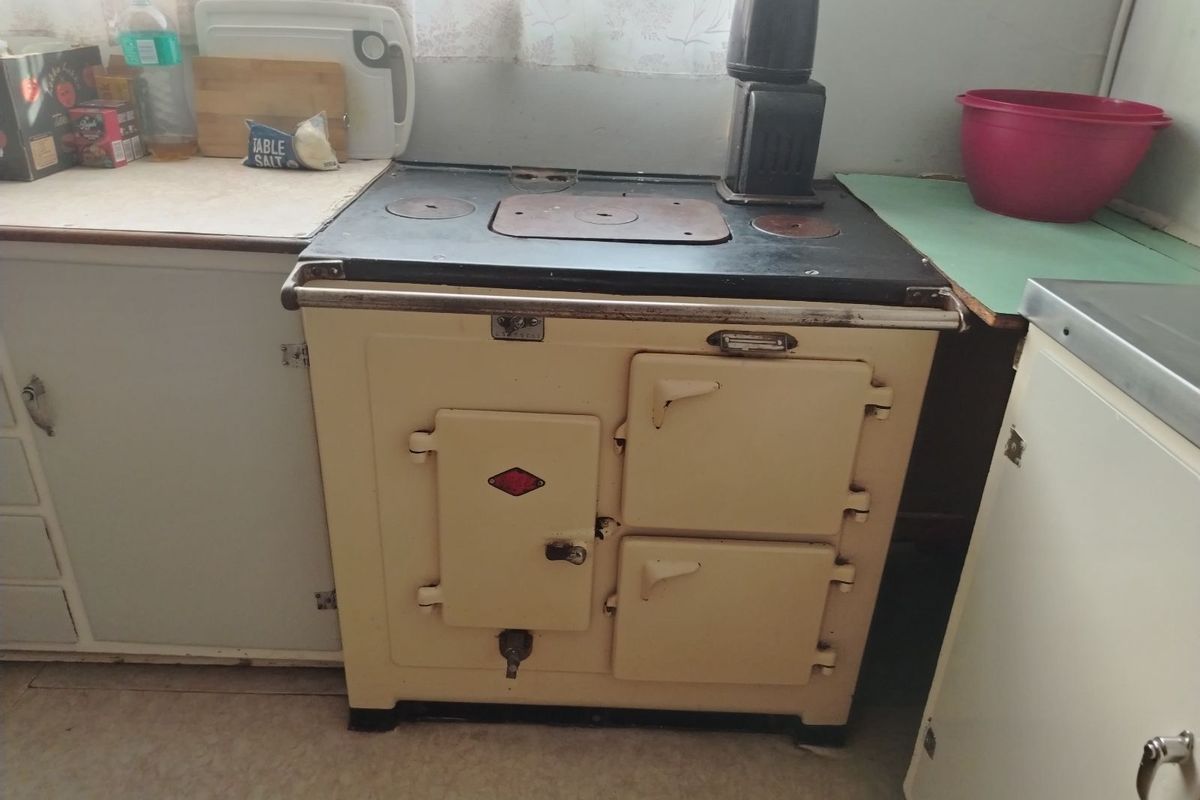 A dated kitchen area featuring a vintage-style solid fuel or electric range cooker and basic cabinetry with worn surfaces.
