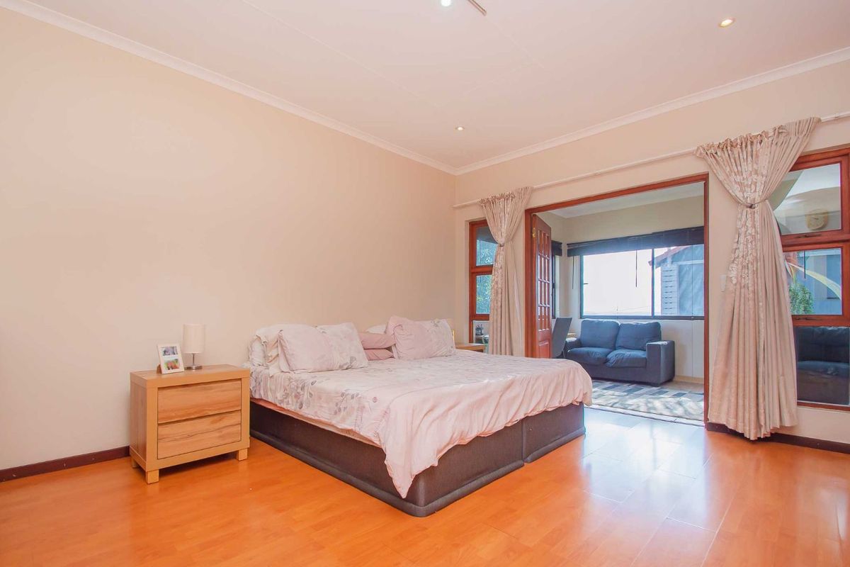 Spacious bedroom featuring warm-toned laminate flooring, recessed ceiling lighting, and direct access to an adjoining sunroom through large wooden-framed glass doors.