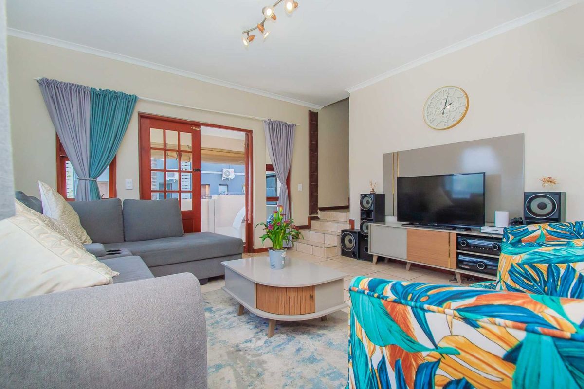 A comfortable living room featuring tiled flooring, a built-in media wall unit, and direct access to an outdoor patio area through wooden French doors.