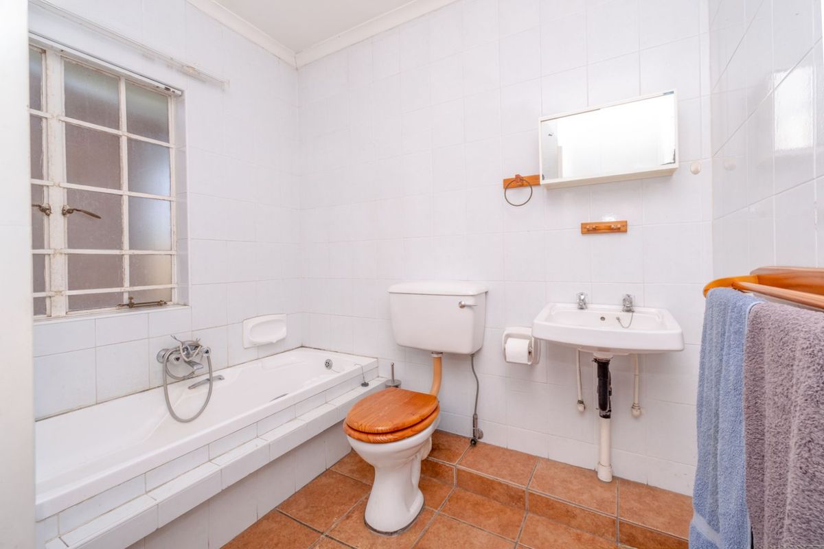 A functional bathroom featuring a built-in bathtub, wall-mounted basin, and toilet with white wall tiling and terracotta floor tiles.