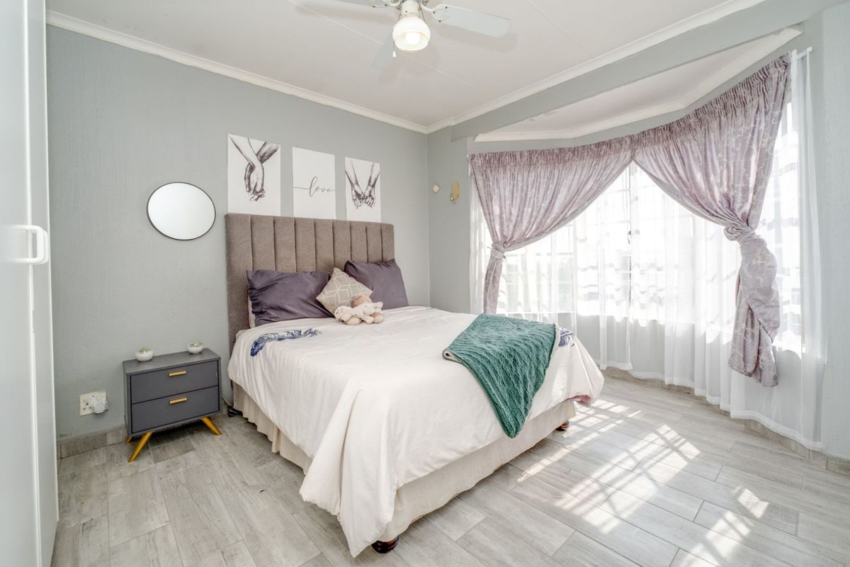 A bright and well-maintained bedroom featuring light-toned tiled flooring, a ceiling fan, and a large bay window that allows for ample natural light.