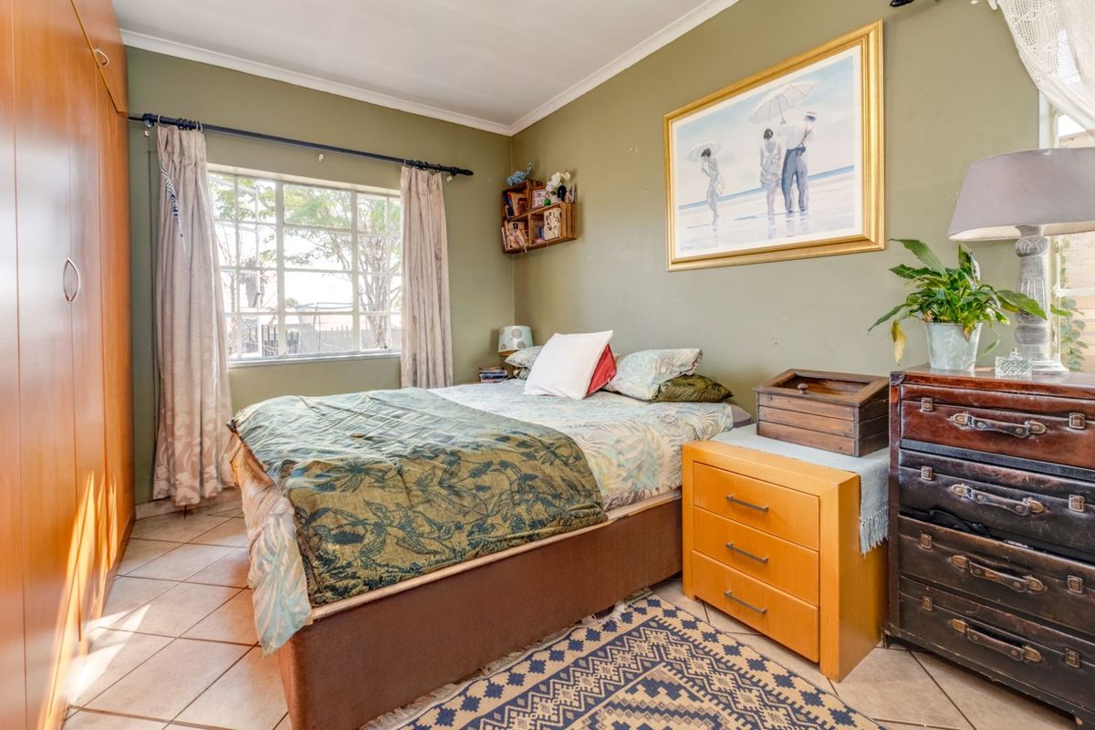 A bedroom featuring built-in wooden cupboards, tiled flooring, and a large window allowing natural light into the space.