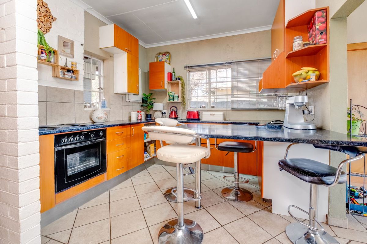A functional kitchen featuring wooden cabinetry, dark laminate countertops, a built-in oven, and a breakfast bar area with tiled flooring.