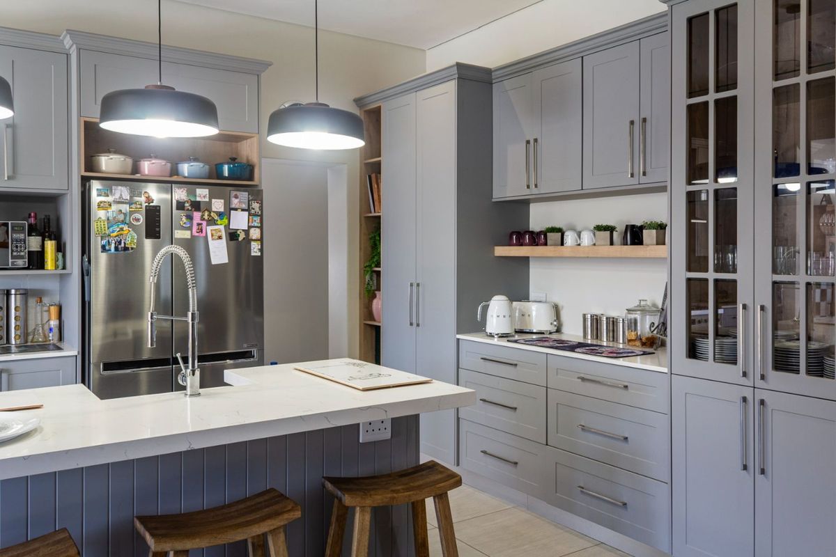 Modern kitchen featuring grey shaker-style cabinetry, stone countertops, a central island with a prep sink, and integrated storage solutions.