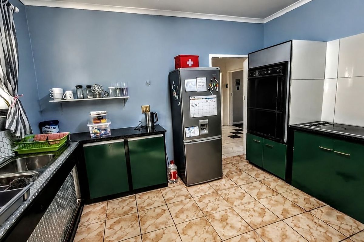 A functional kitchen featuring green cabinetry, dark countertops, a built-in double oven, and a stainless steel double sink with a tiled backsplash.