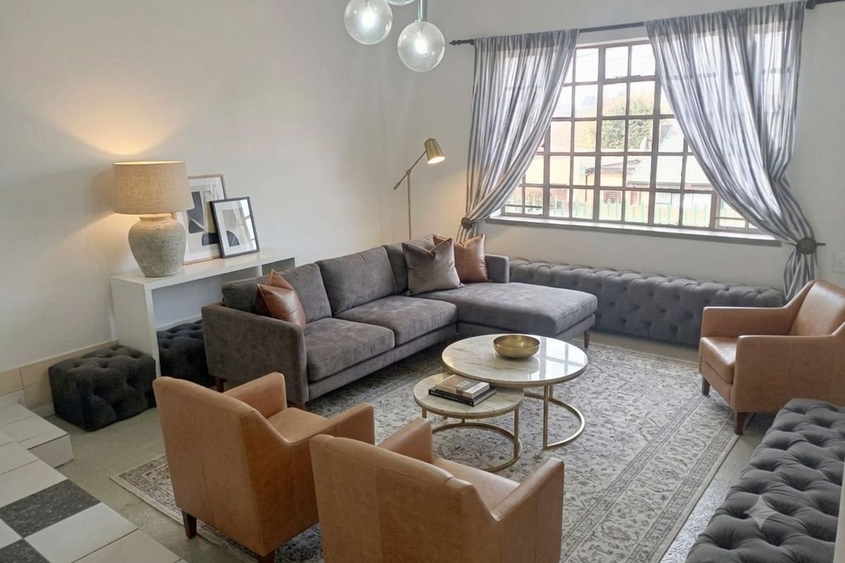 A well-lit living room featuring a large window with grid detailing, modern pendant lighting, and tiled flooring.