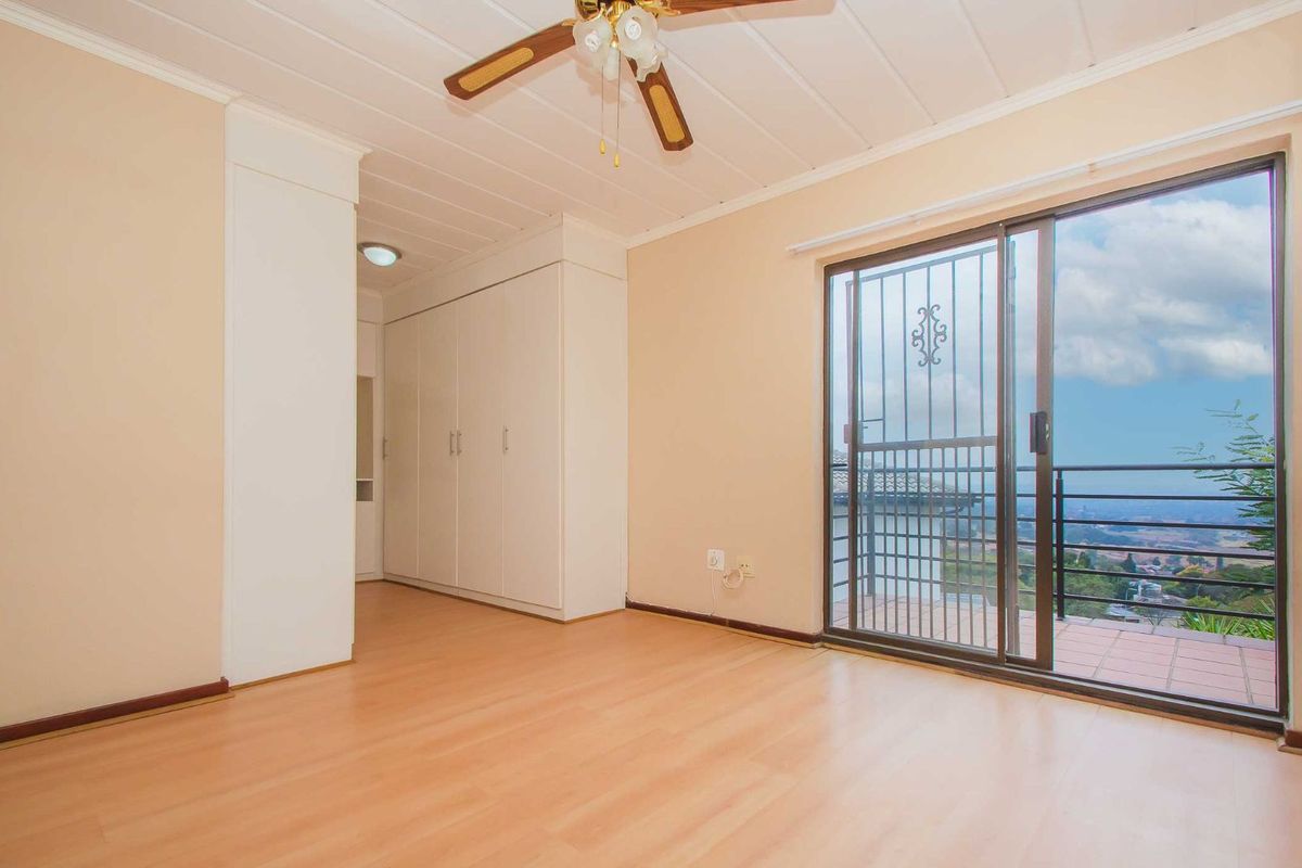 A bright bedroom featuring built-in wardrobes, laminate flooring, a ceiling fan, and sliding glass doors opening onto a balcony with scenic views.