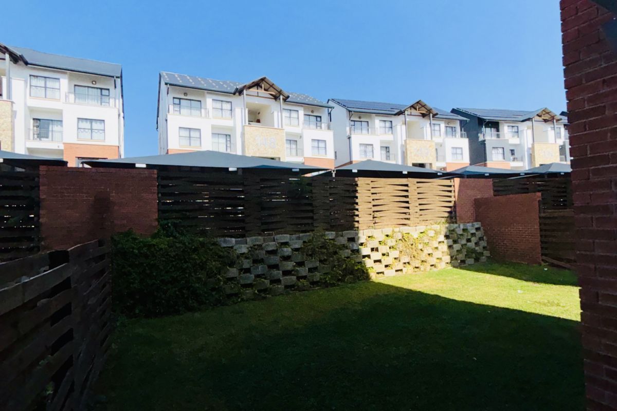 A private rear garden area featuring a lawn, enclosed by timber fencing and a brick retaining wall, with views of the surrounding apartment complex.