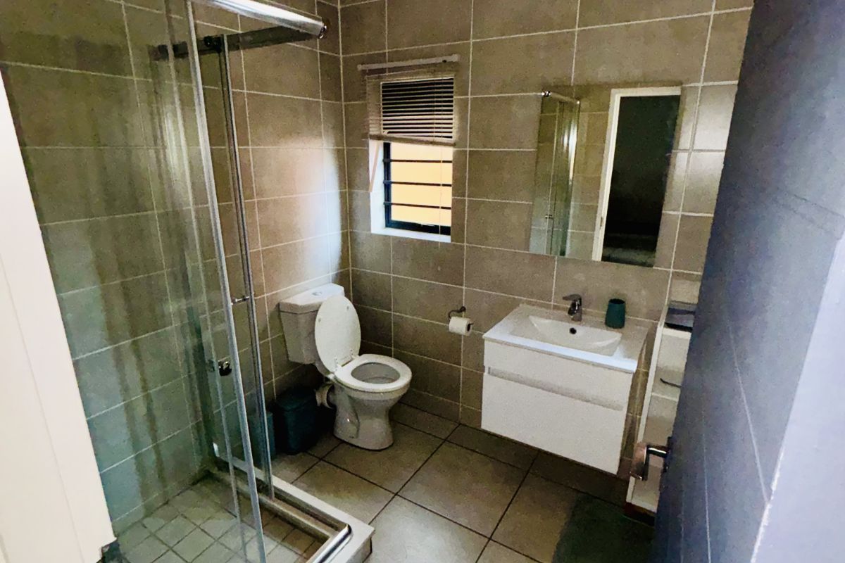 A modern bathroom featuring a glass-enclosed shower, wall-mounted vanity with basin, and tiled flooring and walls.