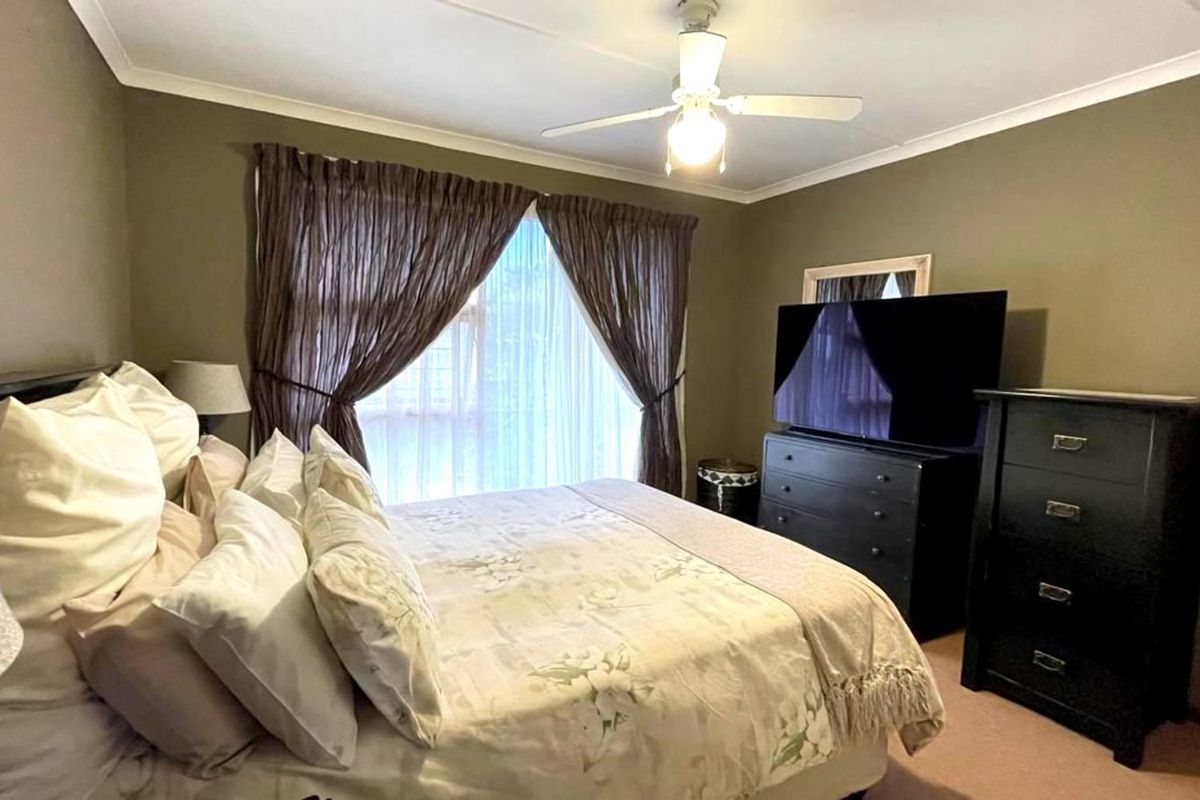 A comfortable bedroom featuring a ceiling fan and large window with curtains, providing a functional and well-maintained living space.
