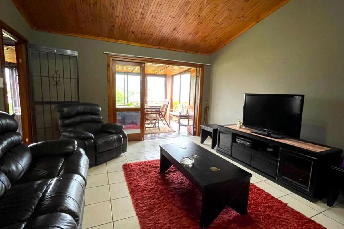 Spacious living room featuring a vaulted timber ceiling, tiled flooring, and sliding glass doors providing direct access to an enclosed patio area.