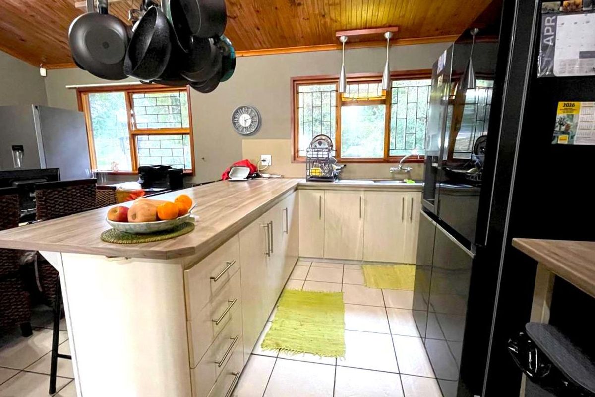 A functional kitchen featuring a breakfast bar, light-toned cabinetry, tiled flooring, and a timber-paneled ceiling with integrated lighting.
